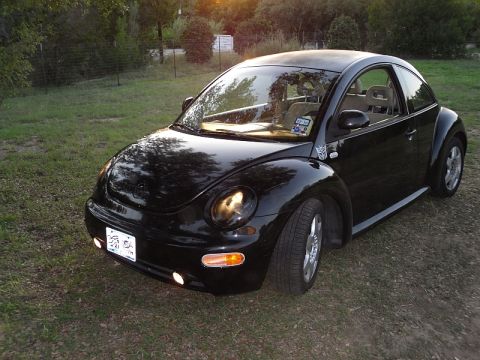 1999 Volkswagen Beetle - This black Volkswagen Beetle is parked outdoors on a grassy area during sunset.
