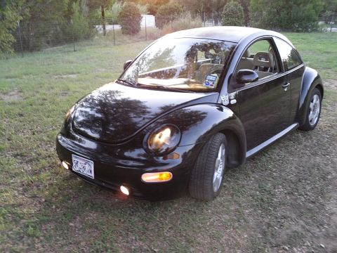 1999 Volkswagen Beetle - A black 1999 Volkswagen Beetle is parked outdoors on a grassy area with gravel.