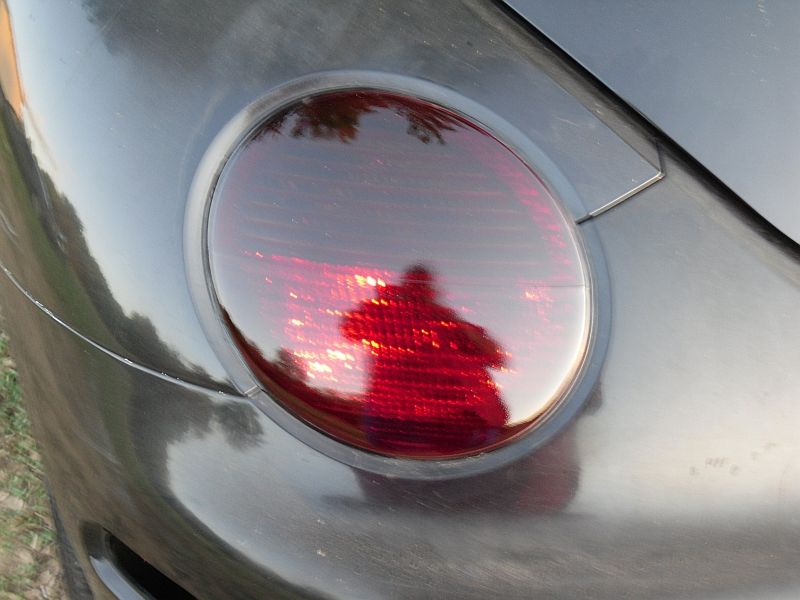 Close-up of a car's red taillight with a reflection of a person
