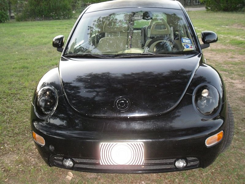 Black Volkswagen Beetle parked on grass. Front view shows headlights, grille, and license plate