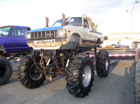 1987 Suzuki Samurai - A heavily modified pickup truck, presented as a monster truck, is parked outdoors next to another vehicle.