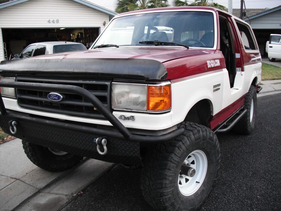 Red and white 1991 Ford Bronco with aftermarket bumper and side steps