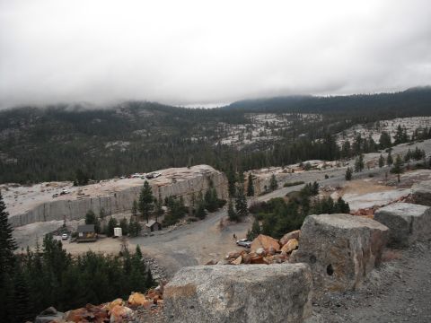 1991 Ford Bronco - A wide shot captures a quarry operation with vehicles and structures amidst a mountainous, forested terrain under an overcast sky.