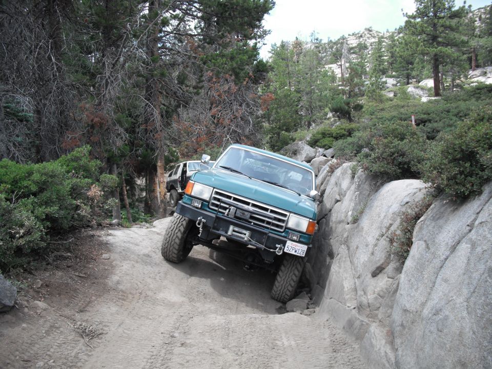 Teal Ford Bronco navigating a narrow, rocky off-road trail with another vehicle behind it