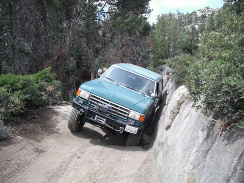 1991 Ford Bronco - This Ford F-Series truck is shown off-roading on a dirt path with large rocks on the side.