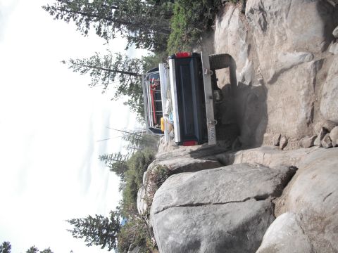 1991 Ford Bronco - A dark blue SUV navigates a challenging rocky trail, with its rear end visible and a license plate reading 5Y50367.