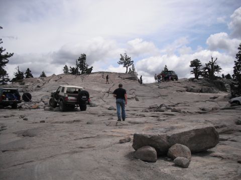 1991 Ford Bronco - Several off-road vehicles are parked on a rocky incline with people milling around.