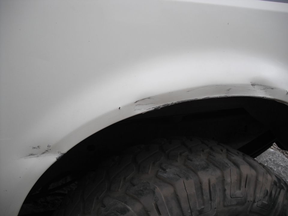Close-up of a white vehicle's rear wheel well showing some scratches and dirt