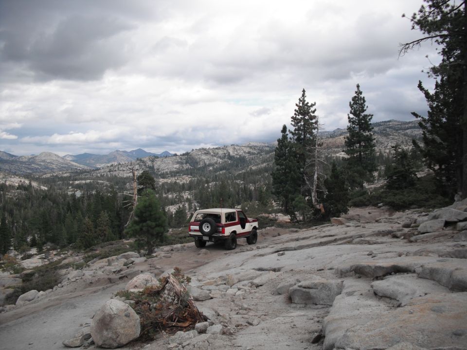 White and red SUV with spare tire on rear door, driving on a rocky, mountainous terrain