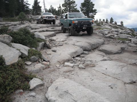1991 Ford Bronco - Two modified off-road vehicles tackle a challenging rocky path in a mountainous area.