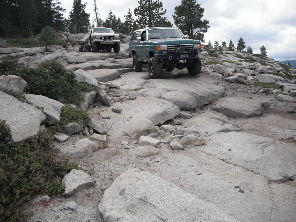 1991 Ford Bronco and a white pickup truck navigating a rocky trail