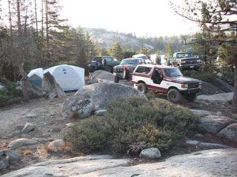 1991 Ford Bronco - Several off-road vehicles and tents are set up at a campsite in a rocky, wooded area.