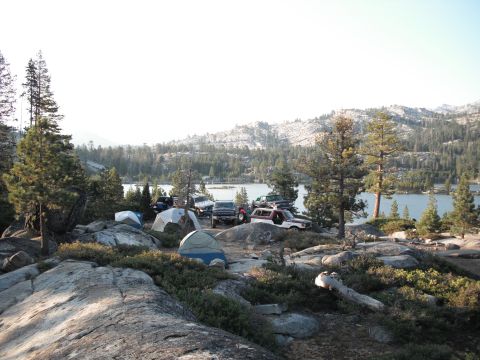 1991 Ford Bronco - Multiple vehicles and tents set up at a lakeside campsite surrounded by trees and rocks.