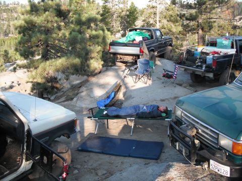 1991 Ford Bronco - A campsite scene with multiple trucks and a person resting on a cot.