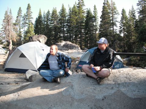 1991 Ford Bronco - Two men relax near tents in a wooded campsite.