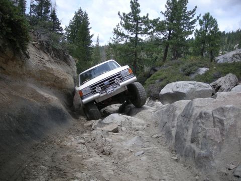 1991 Ford Bronco - This white Ford Bronco is tackling a challenging off-road course with large rocks and steep inclines.