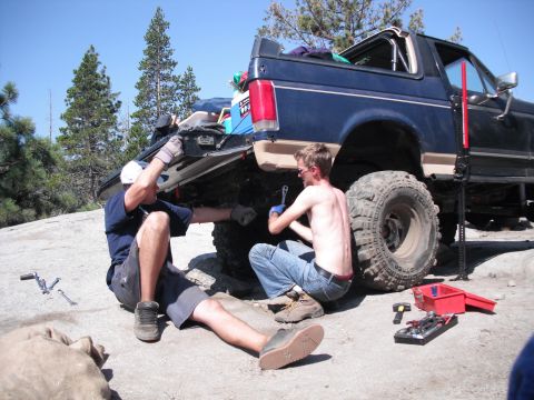 1991 Ford Bronco - Two men are working on the rear suspension of a modified SUV, possibly during an off-road excursion.
