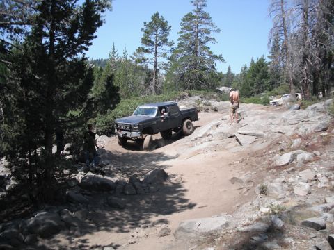1991 Ford Bronco - A modified Ford F-Series truck navigates a challenging off-road path surrounded by trees and rocks.