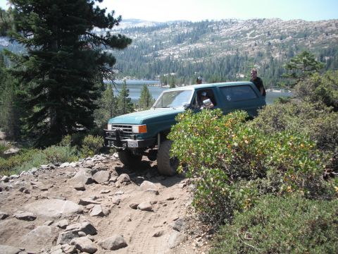 1991 Ford Bronco - A green 1991 Ford Bronco navigates a , rocky trail with a scenic lake and mountains in the distance.