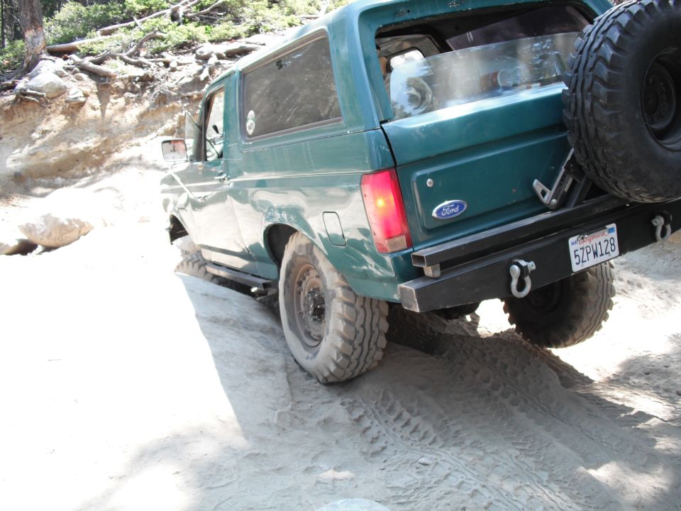 Green Ford Bronco on dirt road, rear view, spare tire mounted on back