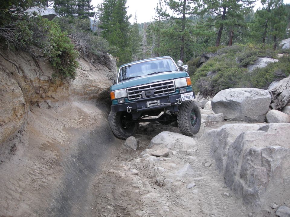 1991 Ford Bronco navigating a difficult rocky off-road path with steep dirt walls