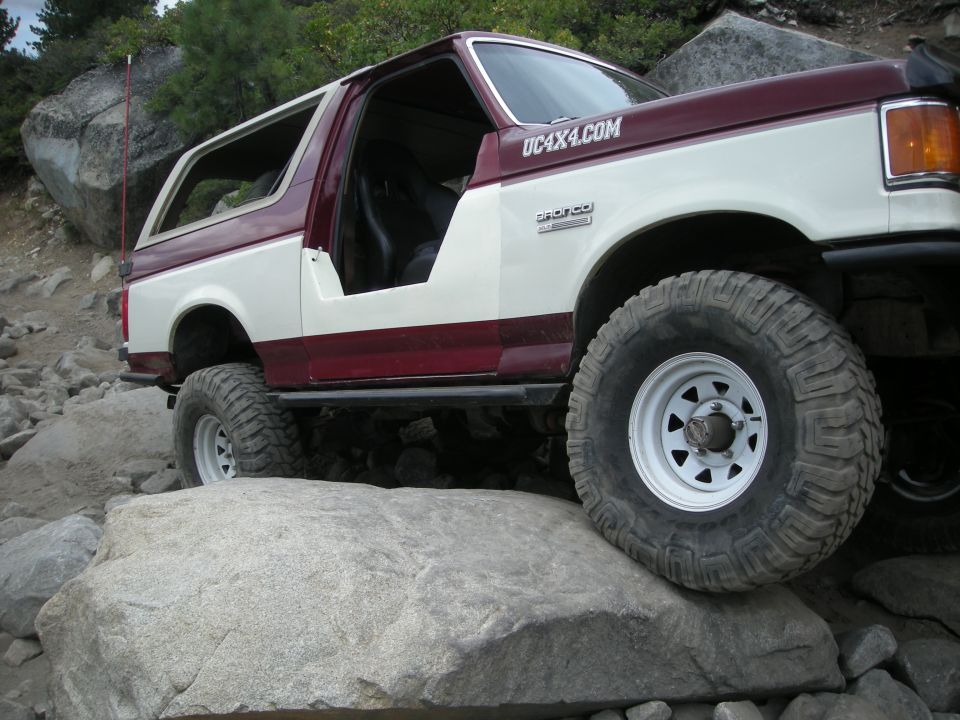Two-tone Ford Bronco with off-road tires navigating large rocks. UC4X4.COM sticker on the side
