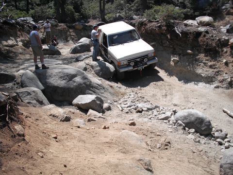 1991 Ford Bronco - A white 1989 Ford Bronco navigates a challenging rocky off-road course with several people observing.