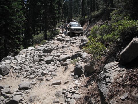 1991 Ford Bronco - A white 1990 Ford Bronco navigates a challenging, boulder-strewn path through a forest.