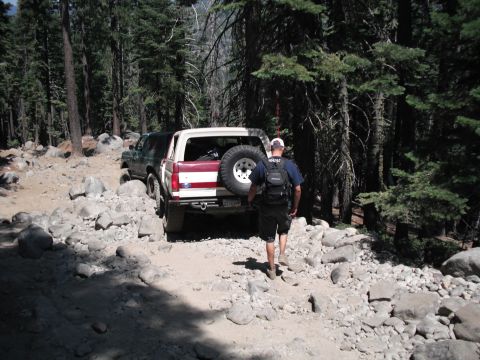 1991 Ford Bronco - A red and white Ford Bronco navigates a rocky trail, with another SUV visible behind it.
