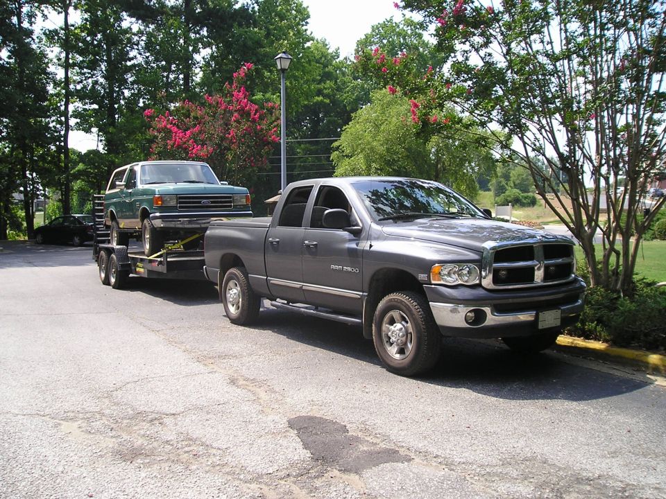 Green 1990s Ford Bronco on a trailer, towed by a gray Dodge Ram pickup truck