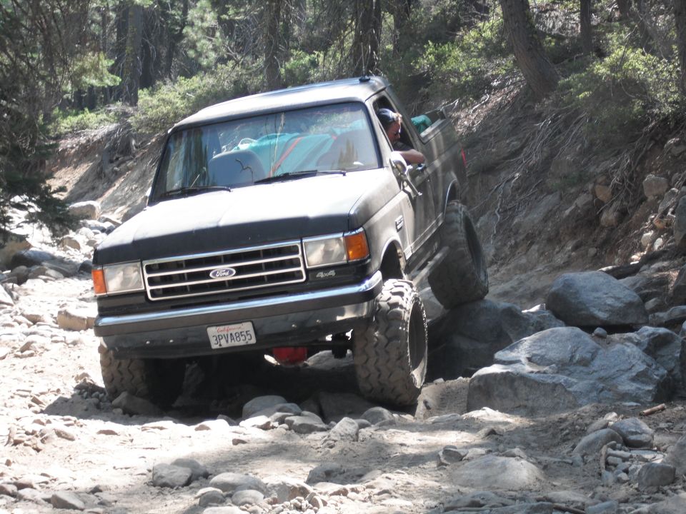 1991 Ford Bronco navigating a rocky trail, front grille visible with 'Ford' and '4x4' badges. License plate reads 3PVA855