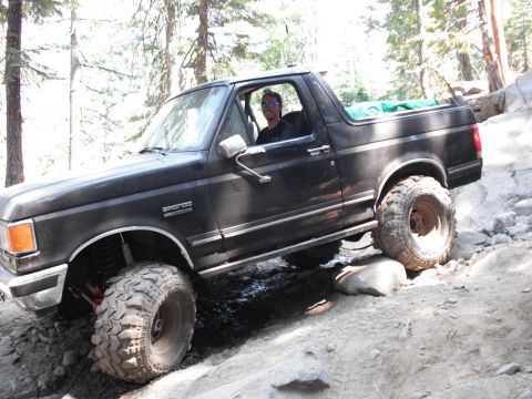 1991 Ford Bronco - Driver navigates a black 1991 Ford Bronco over rocks on an off-road trail.