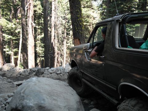 1991 Ford Bronco - A 1991 Ford Bronco navigates a challenging rocky path through a dense forest.