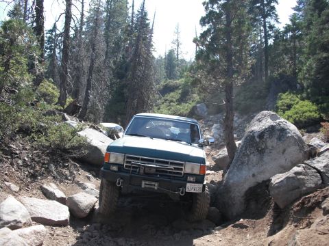 1991 Ford Bronco - This 1980s Ford Bronco is tackling a challenging, rocky path in a wooded area.
