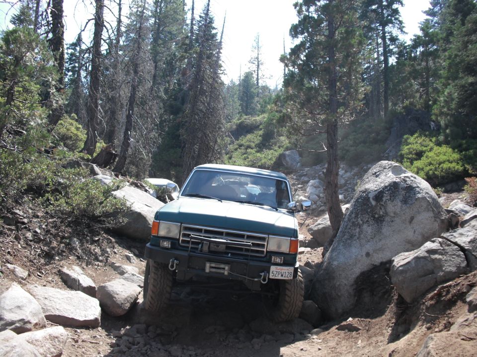 Green 1980s Ford Bronco navigating a rocky off-road trail