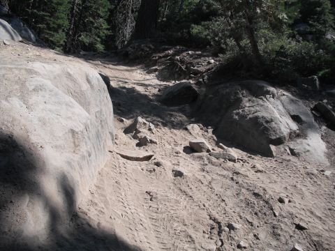 1991 Ford Bronco - A off-road trail winds through a rocky, wooded area with clear tire tracks visible on the dusty path.