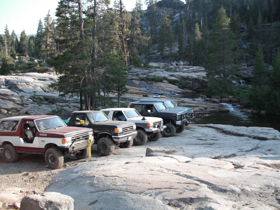 1991 Ford Bronco and three other SUVs parked on rocks near a stream