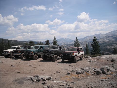 1991 Ford Bronco - Several SUVs are parked on a dirt lot, with a mountainous landscape behind them under a cloudy sky.