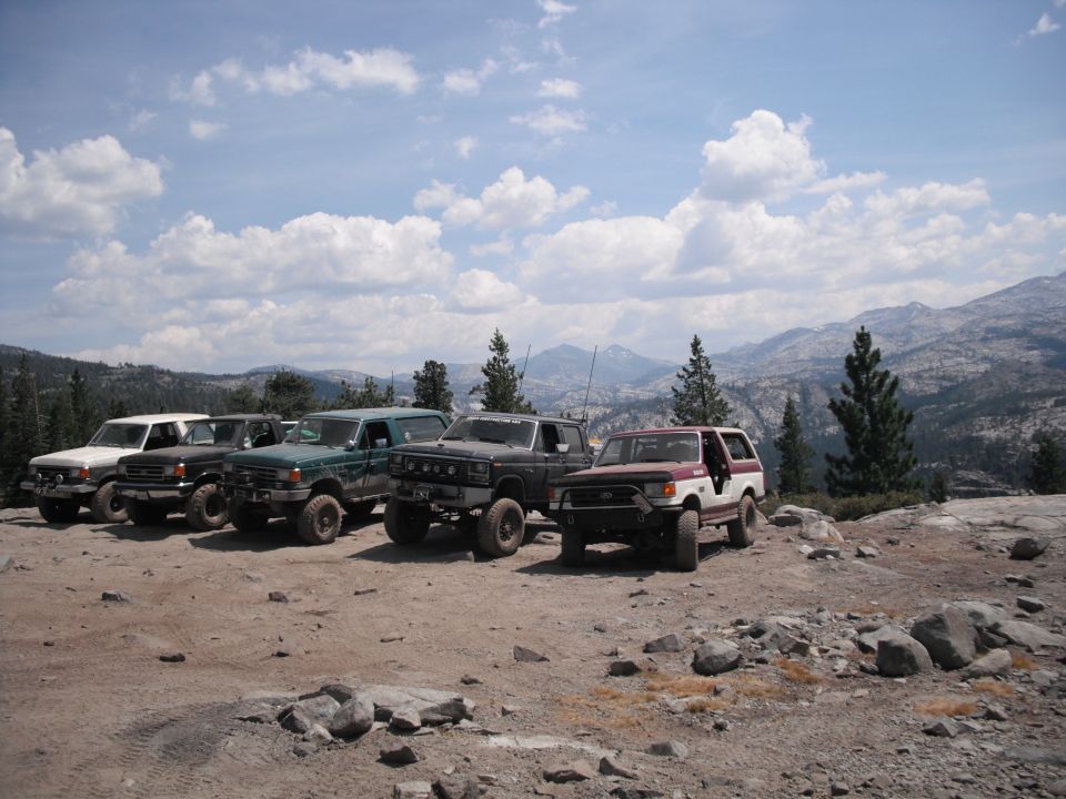 Five off-road SUVs parked on a dirt lot with mountains and trees in the background