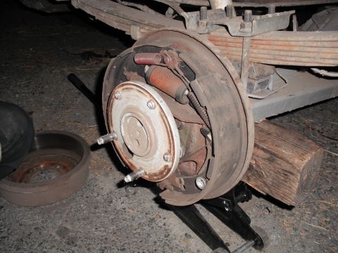 1991 Ford Bronco - Close-up of a vehicle's rear drum brake assembly, supported by a jack and wooden block.