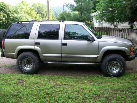 2000 Chevrolet Tahoe - This SUV is parked on a grassy area with trees and a fence in the background. It has a spare tire on the back.