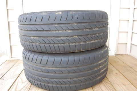 2002 BMW M3 - Two tires are stacked on a wooden surface, with a white-sided building in the background.