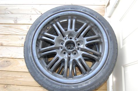 2002 BMW M3 - A single gray alloy wheel with a tire is shown against a wooden background.