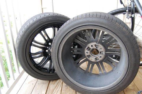 2002 BMW M3 - Two car wheels and tires are shown, one black and one gray, with a bicycle in the background.