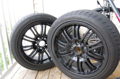 2002 BMW M3 - A pair of black alloy wheels and tires are shown, with a bicycle in the background.