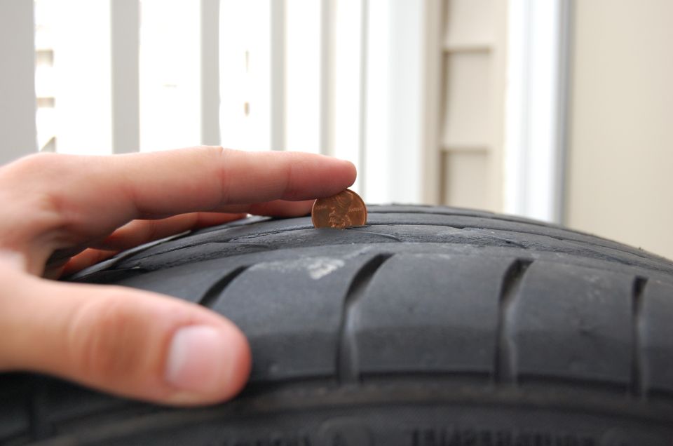 Hand holding penny in tire tread groove to check tread depth