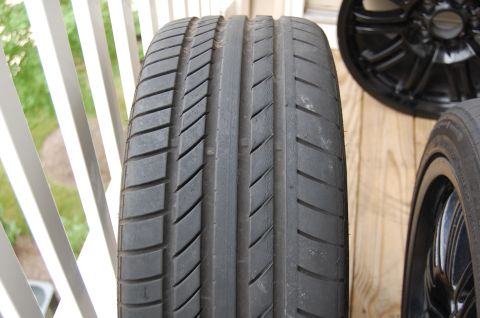 2002 BMW M3 - A tire and a black wheel are shown in detail, with a wooden background and white railing.