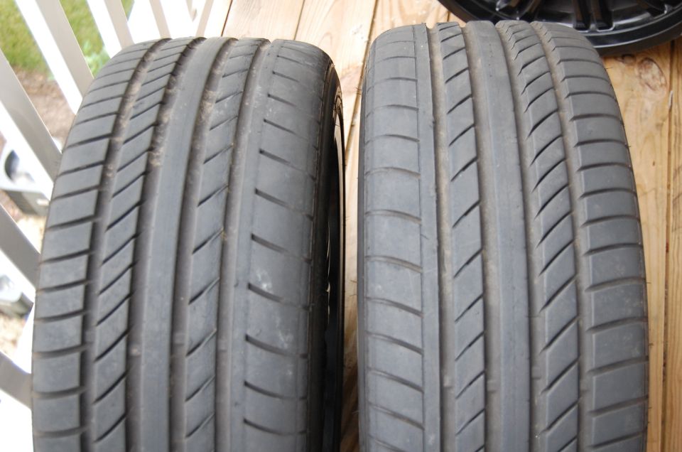 Two car tires side-by-side on a wooden surface. A black rim is visible in the upper right