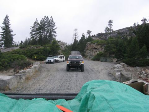1989 Ford Bronco - A red pickup truck with an aftermarket bumper is seen from the front on a gravel road, with other vehicles parked ahead.