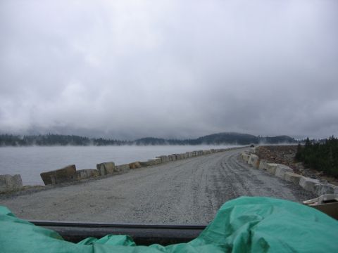 1989 Ford Bronco - A car drives on a gravel road beside a misty lake on an overcast day.